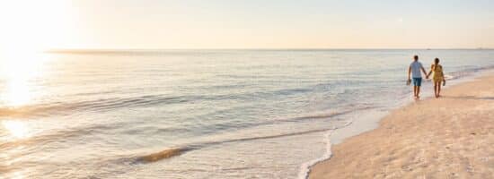 a couple walk hand-in-hand at the beach on a sunny day